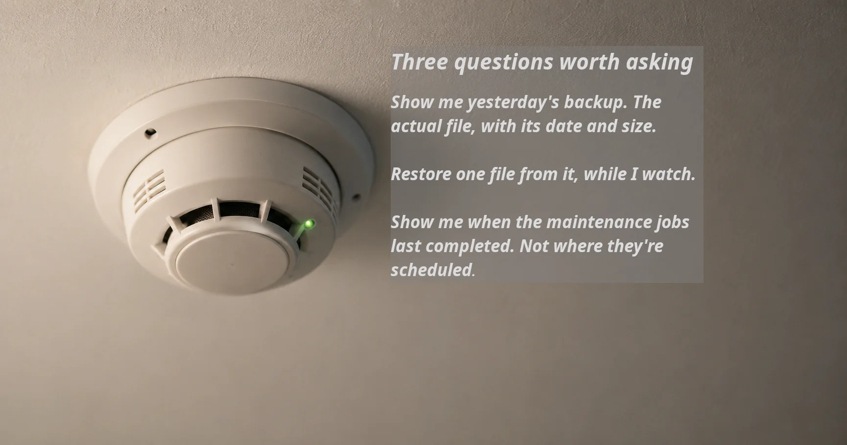 A white ceiling-mounted smoke detector with a glowing green status light. To the right, a heading reads "Three questions worth asking," followed by three questions: show me yesterday's backup file with its date and size; restore one file from it while I watch; show me when the maintenance jobs last completed, not where they're scheduled.